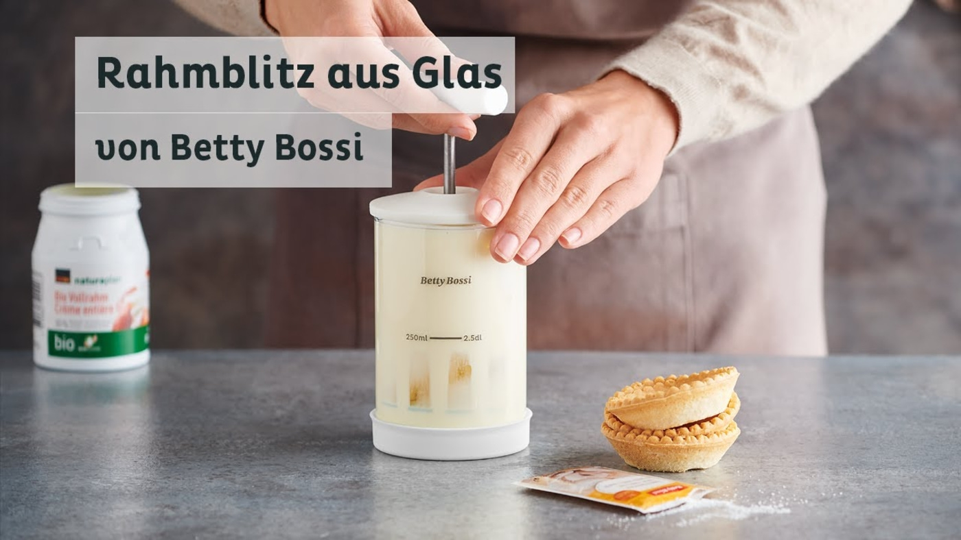 Personne tenant un fouet à crème en verre de Betty Bossi, avec pâtisseries et ingrédients.