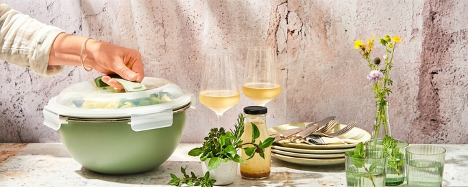 Grüne Schüssel mit Salat, Wein und Kräutern auf Tisch