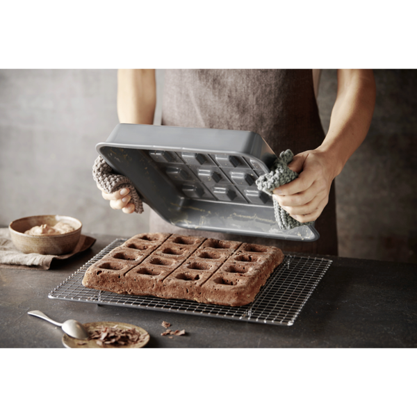 Person hält Backform über Kuchen auf einem Rost, mit Schokoladenstückchen.