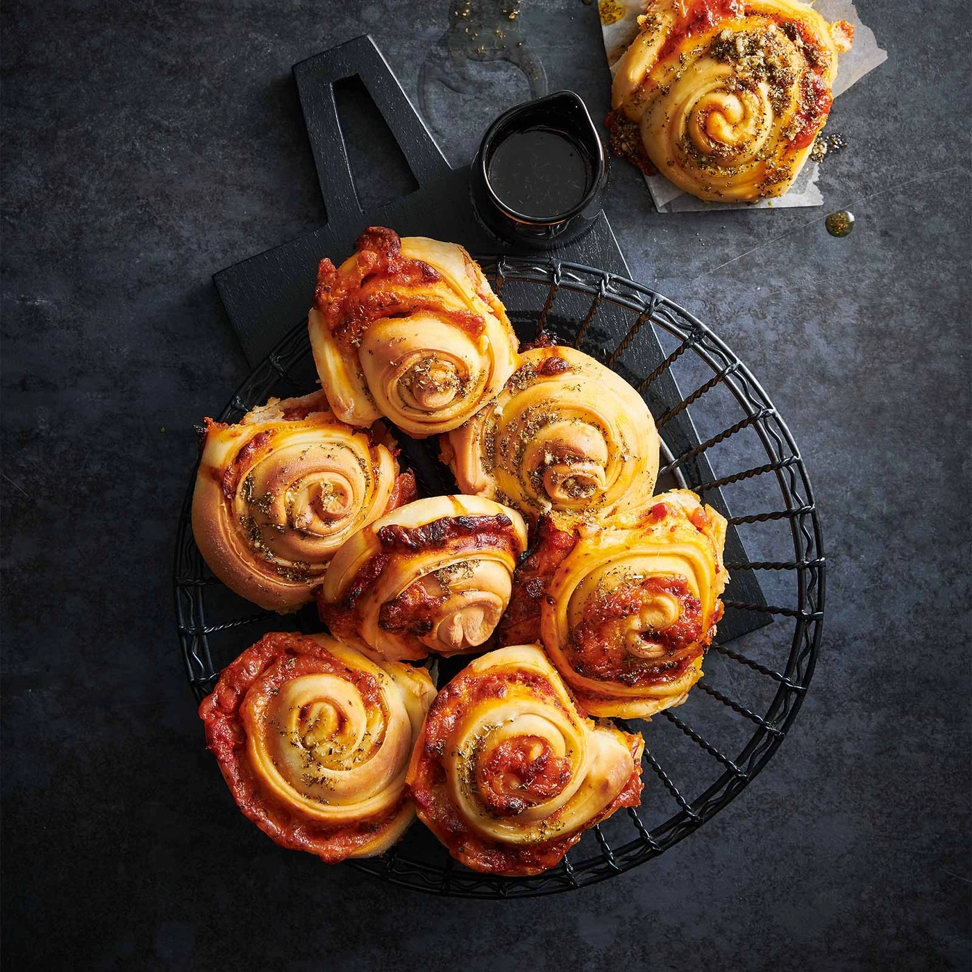 Pizza-Schnecken in einem Korb, mit Soße und Kräutern, auf dunklem Hintergrund.
