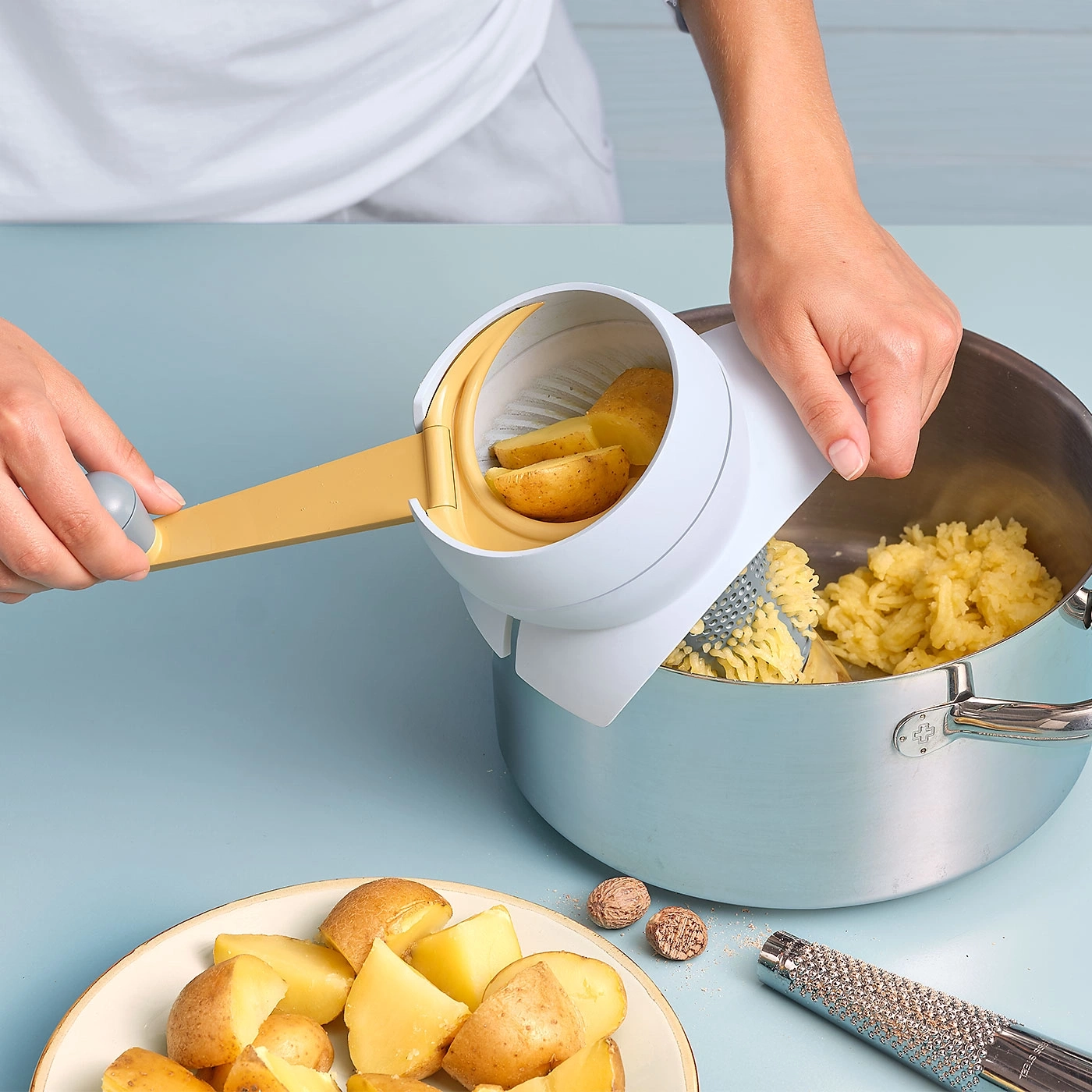 Une personne écrase des pommes de terre avec un presse-purée dans une casserole.