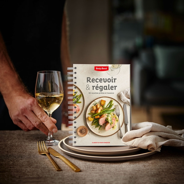Kochbuch mit Essen, Wein und Besteck auf einem Tisch, bereit zum Essen.