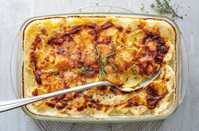Auflauf mit Kartoffeln und Käse, serviert in einer Glasform mit Kräutern