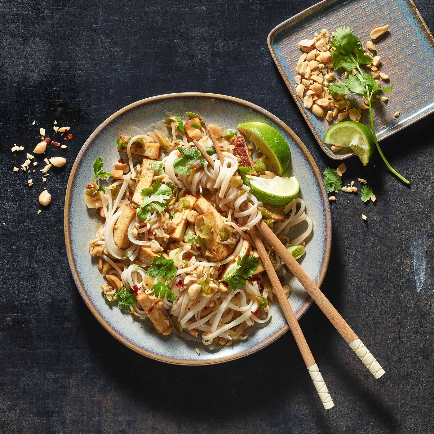 Pad Thai mit Tofu, Erdnüssen, Limette und Koriander auf einem Teller mit Stäbchen