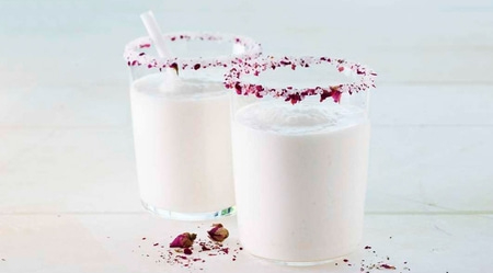 Deux verres avec des pétales de rose sur le bord, boisson laiteuse, fond blanc.