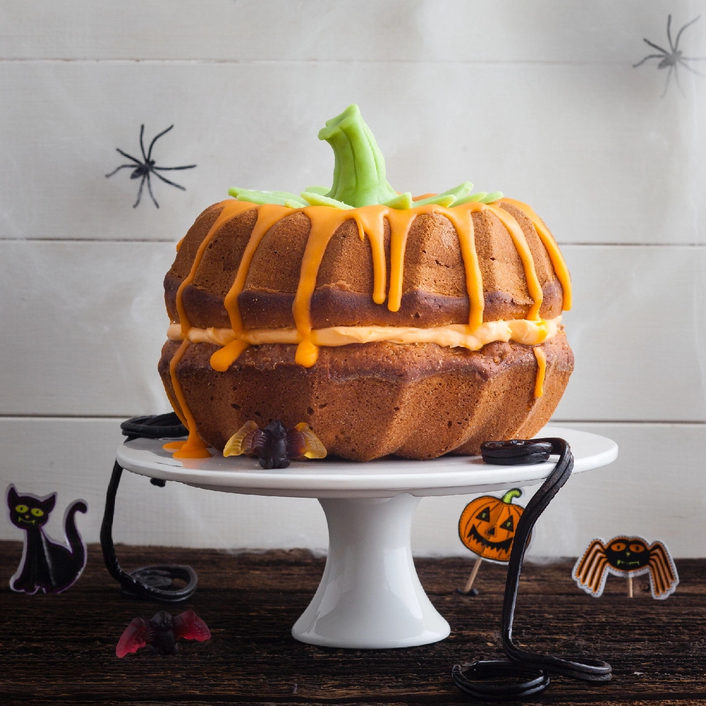 Kürbiskuchen auf einem weißen Ständer mit Halloween-Dekorationen.