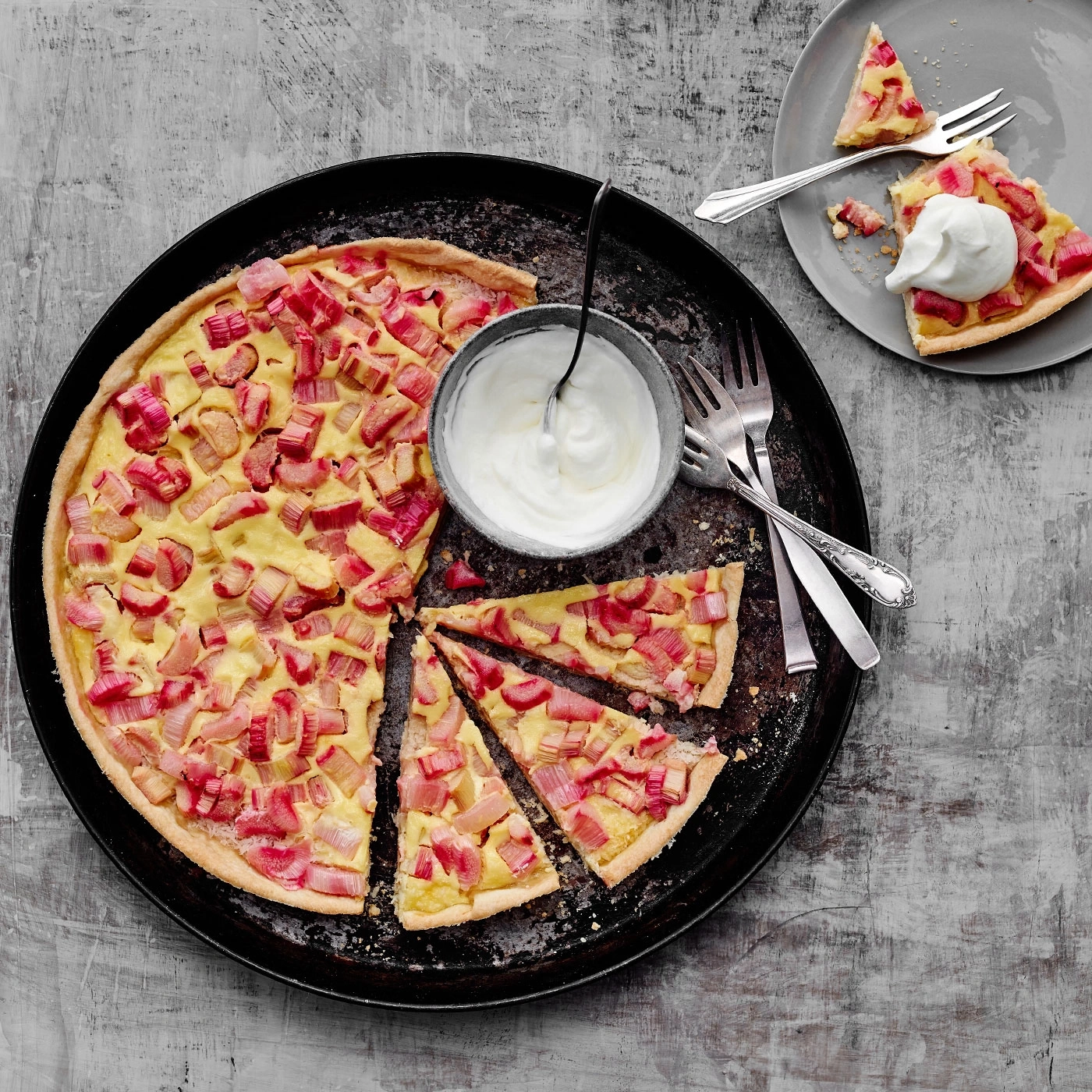 Rhabarberkuchen mit Sahne auf einem Teller, serviert mit Gabeln