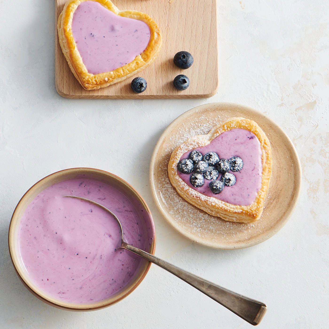 Herzförmiges Gebäck mit Blaubeeren und Creme, auf einem Teller und Brett