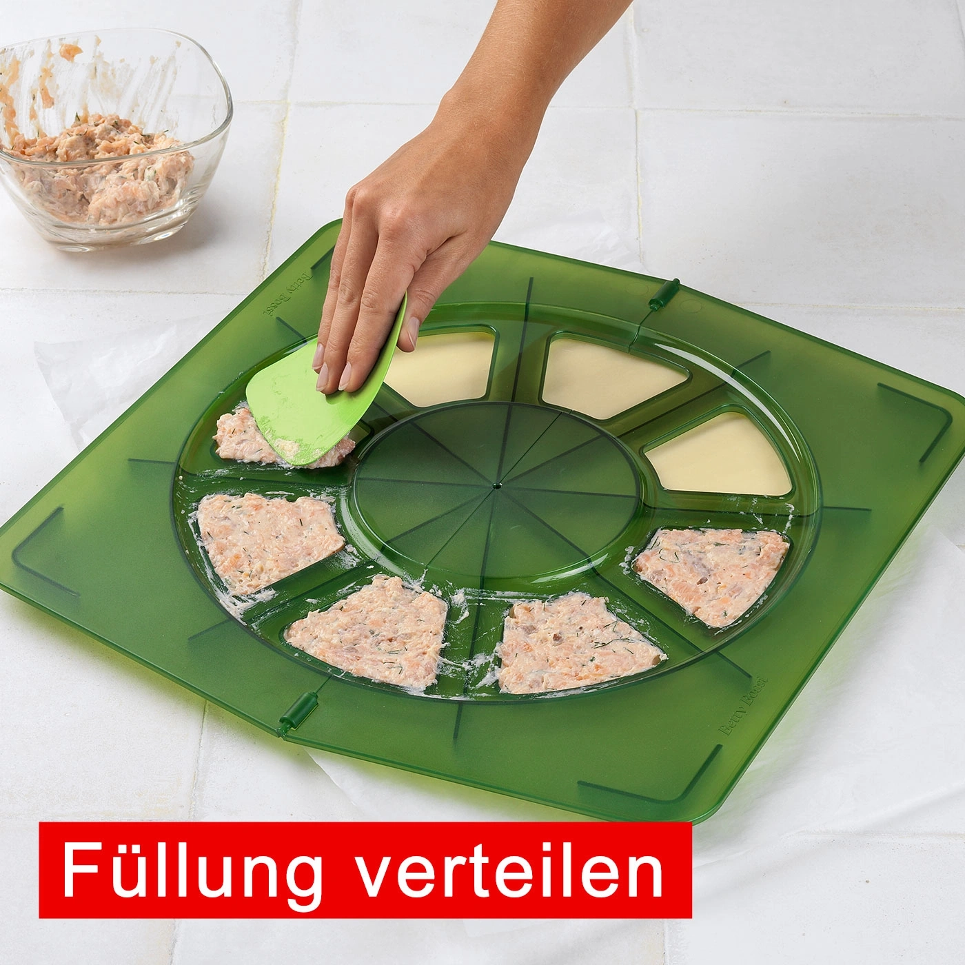 Person verteilt Füllung mit Spatel auf grünem Tablett. Schüssel mit Füllung daneben.