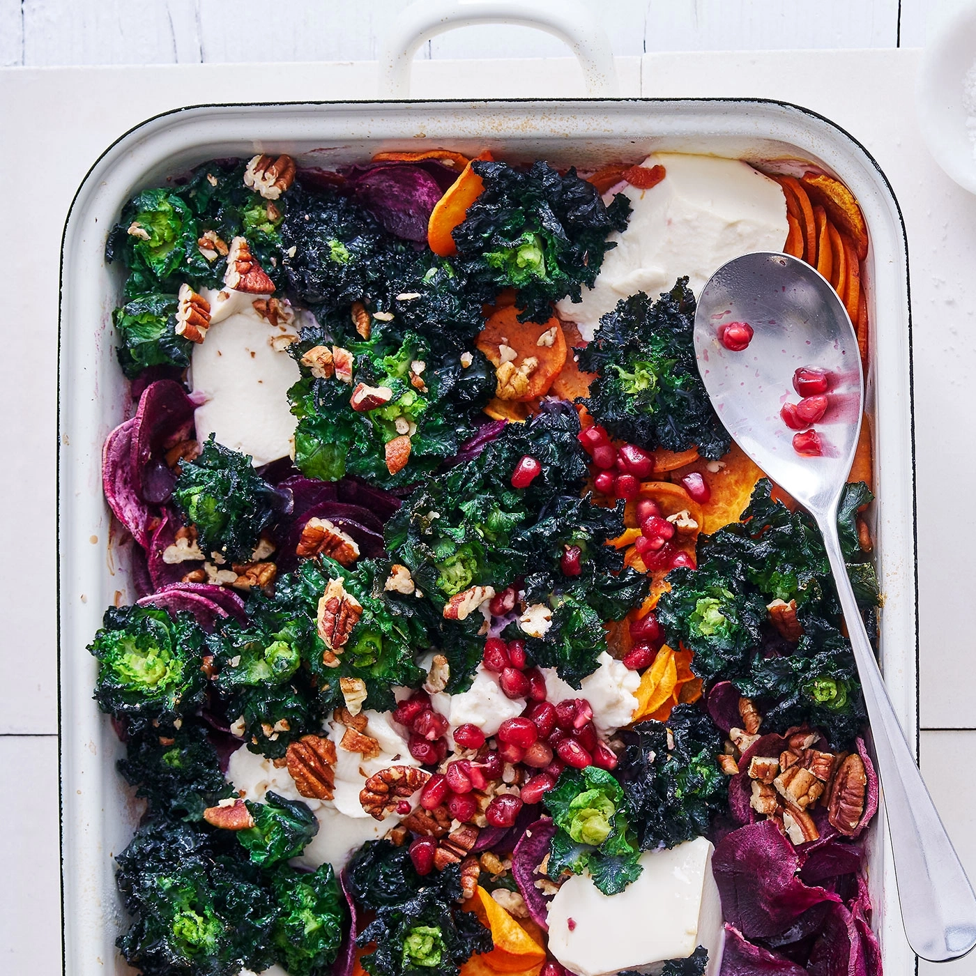 Gratin de légumes rôtis avec graines de grenade, noix et fromage dans un plat.