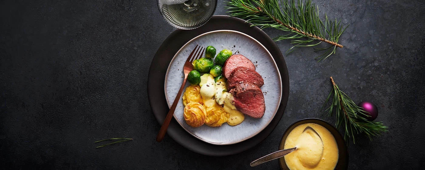 Festliches Gericht mit Fleisch, Gemüse und Sauce, dekoriert mit Tannenzweigen.