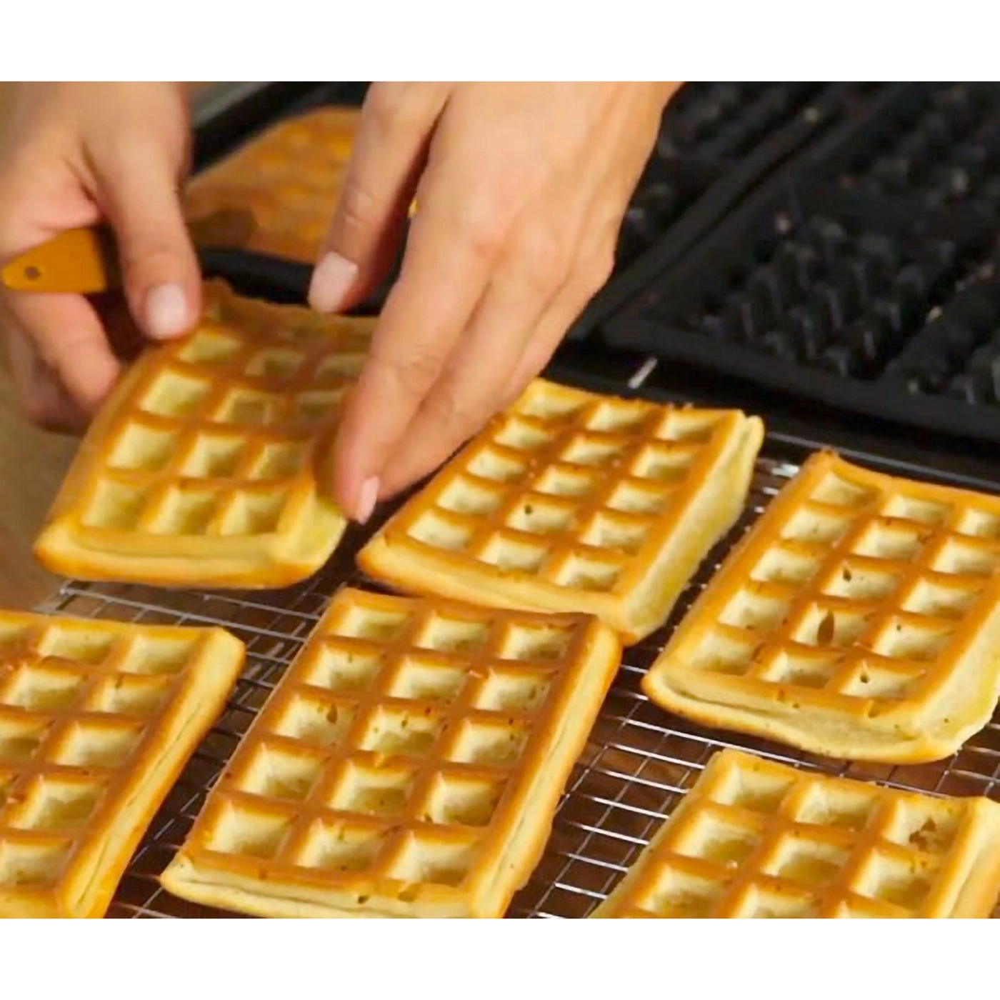 Hände mit Waffeln, die aus einem Waffeleisen genommen werden, auf einem Rost platziert
