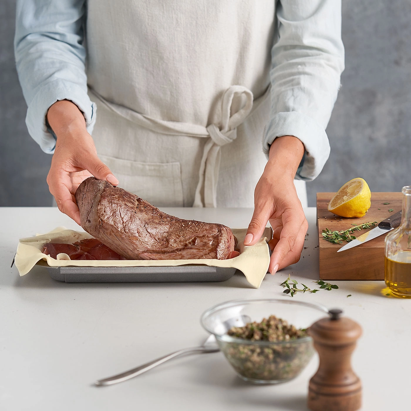 Person bereitet Fleisch zu, mit Zitrone, Kräutern und Gewürzen auf dem Tisch.