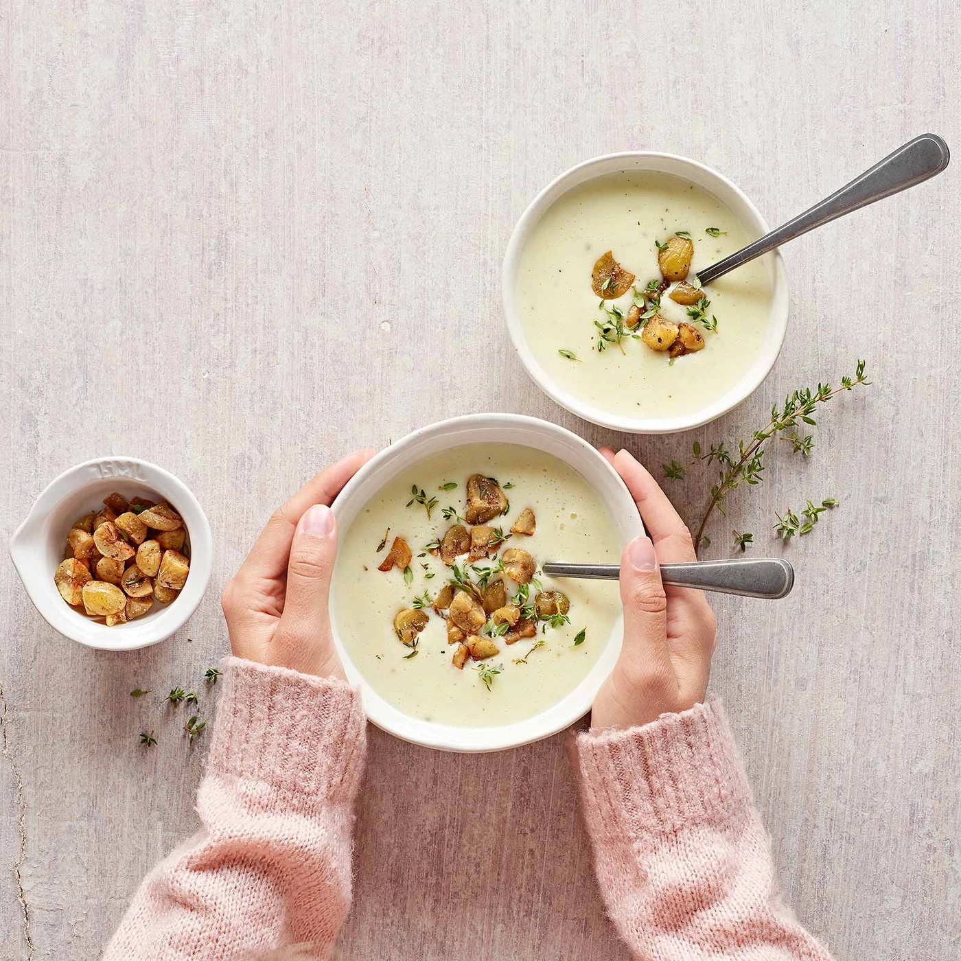Zwei Schüsseln Suppe mit Pilzen und Kräutern, gehalten von Händen in rosa Pullovern.