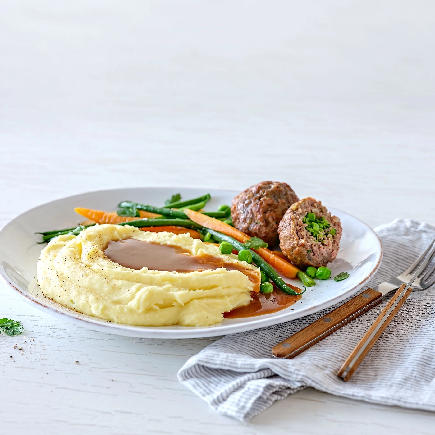 Assiette de boulettes de viande, purée de pommes de terre et légumes, servie avec de la sauce.