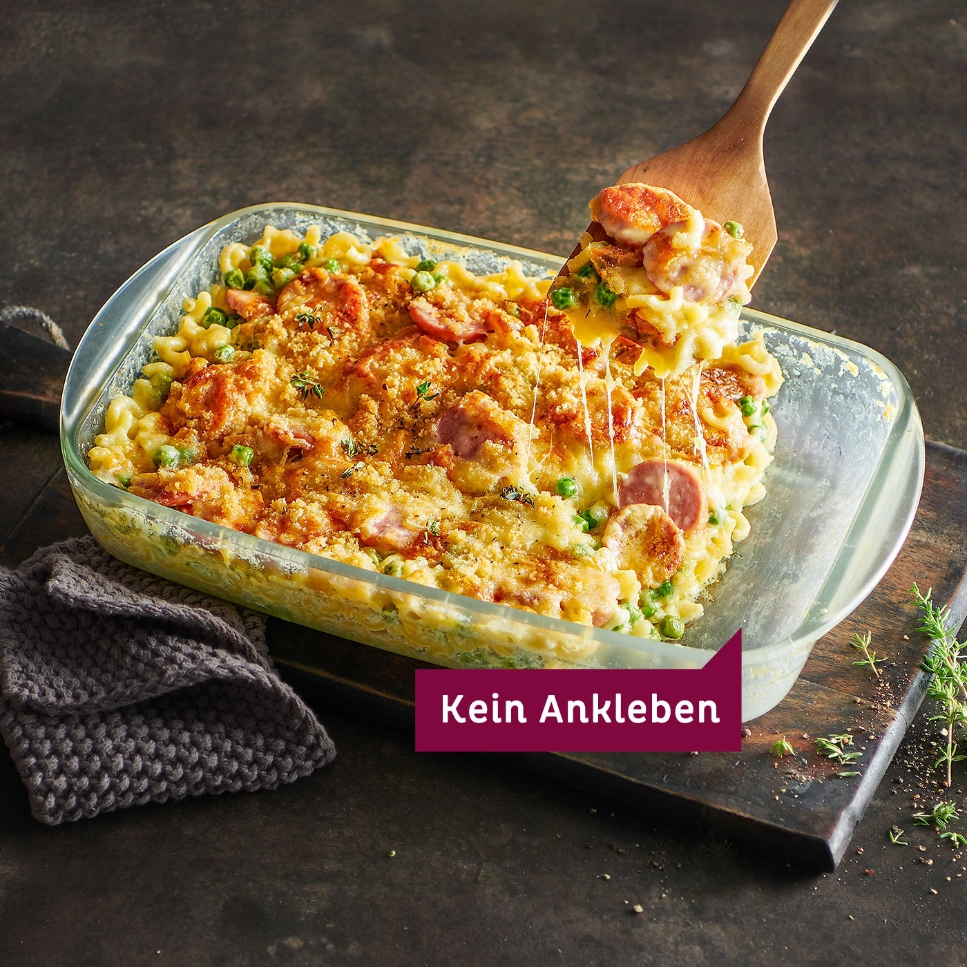 Auflauf mit Wurst, Erbsen und Käse, serviert mit einem Holzlöffel.