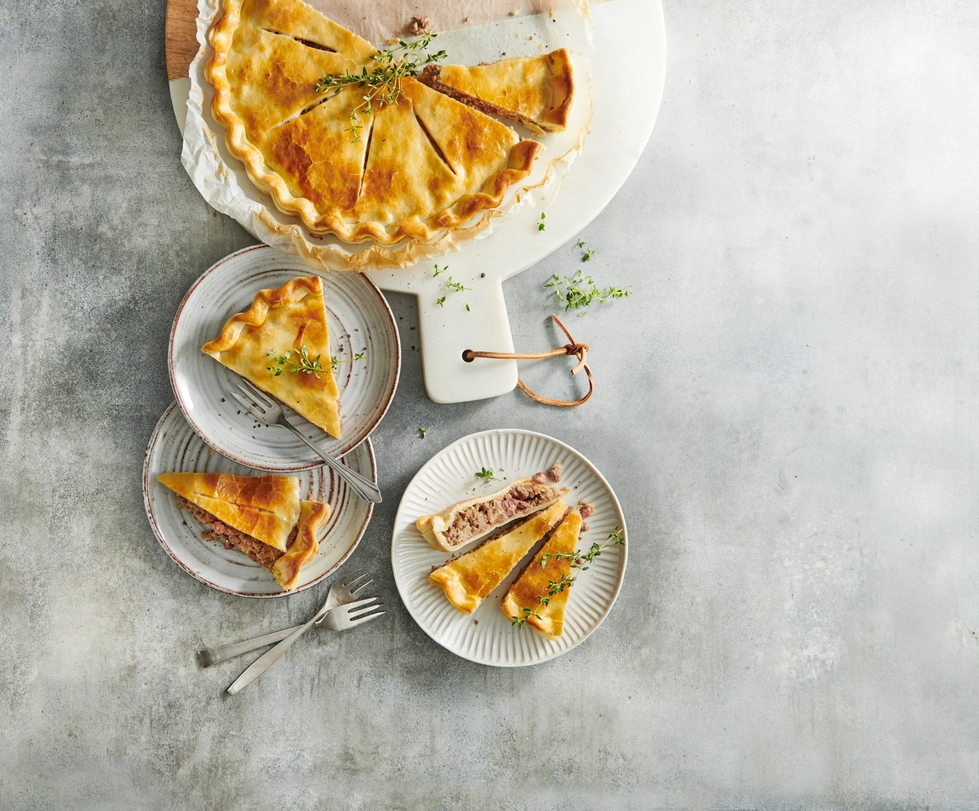 Kuchen, aufgeschnitten, auf Tellern, mit Kräutern, auf grauem Hintergrund, von oben gesehen.