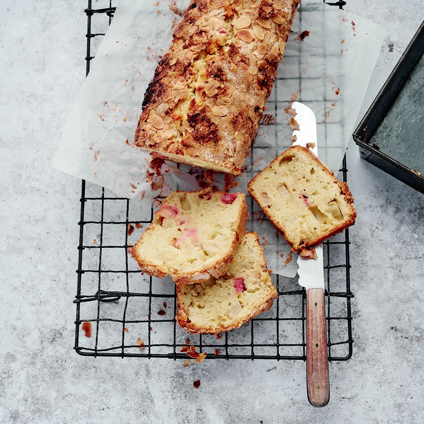 Kuchen mit Mandeln und Rhabarber, auf einem Gitter mit Messer und Backform