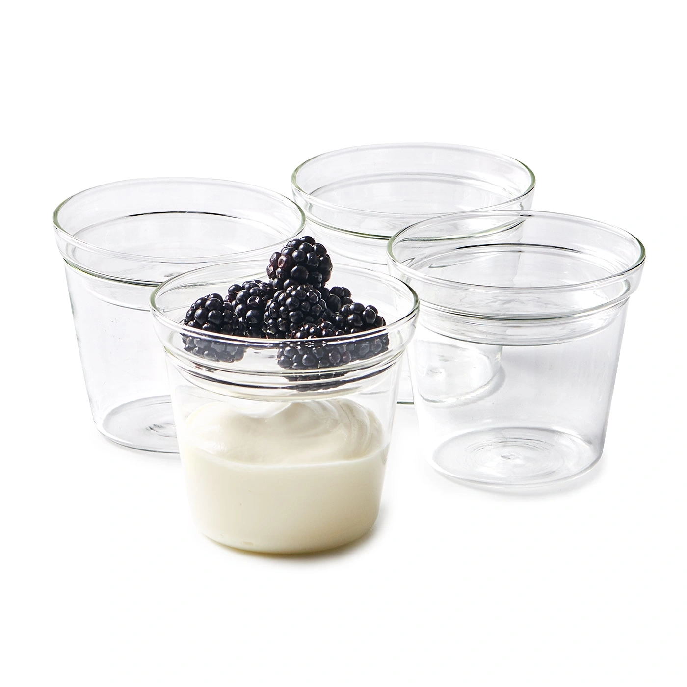 Joghurt mit Brombeeren in Gläsern, umgeben von leeren Gläsern auf weißem Hintergrund.