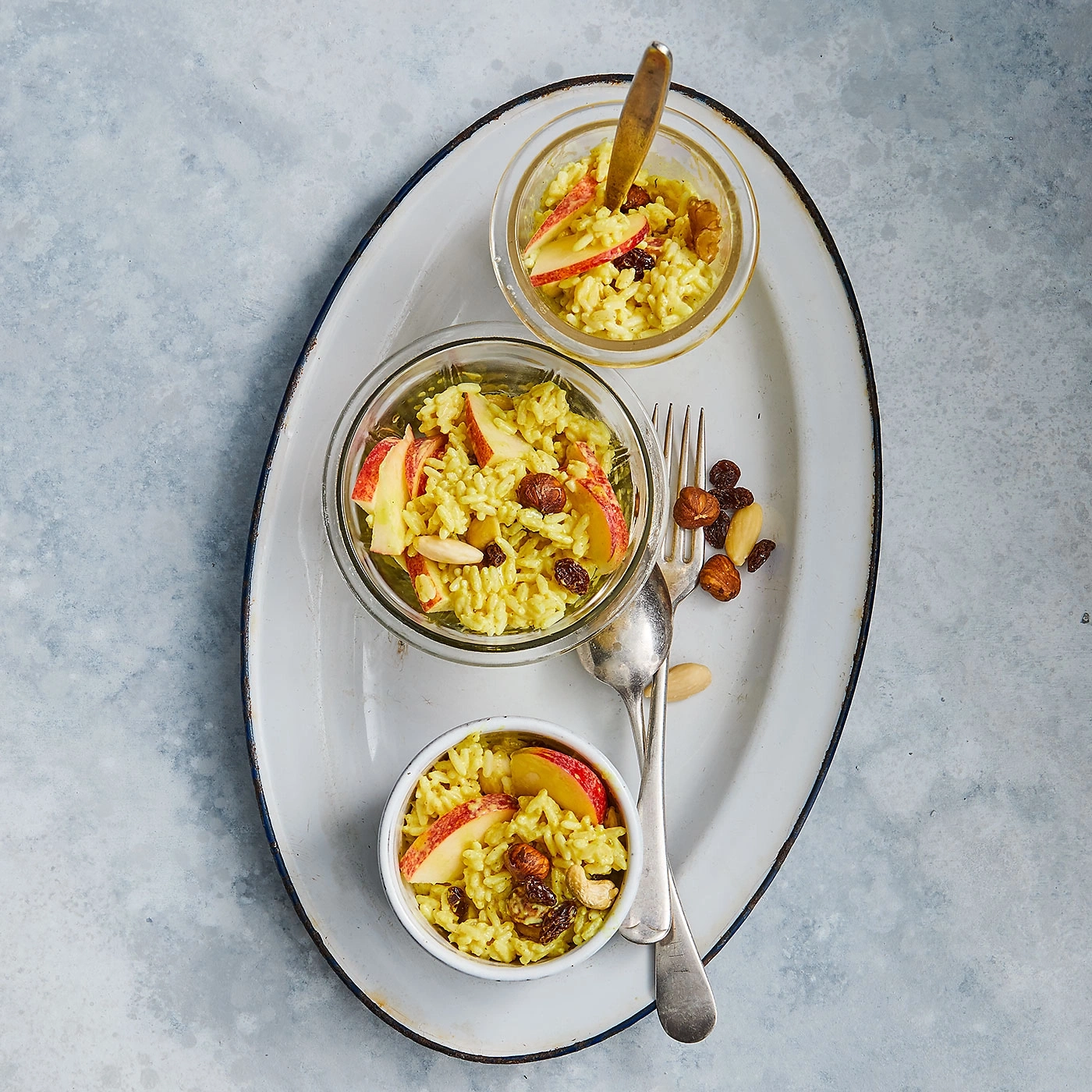 Trois bols de riz aux pommes, raisins secs et noix sur un plateau.