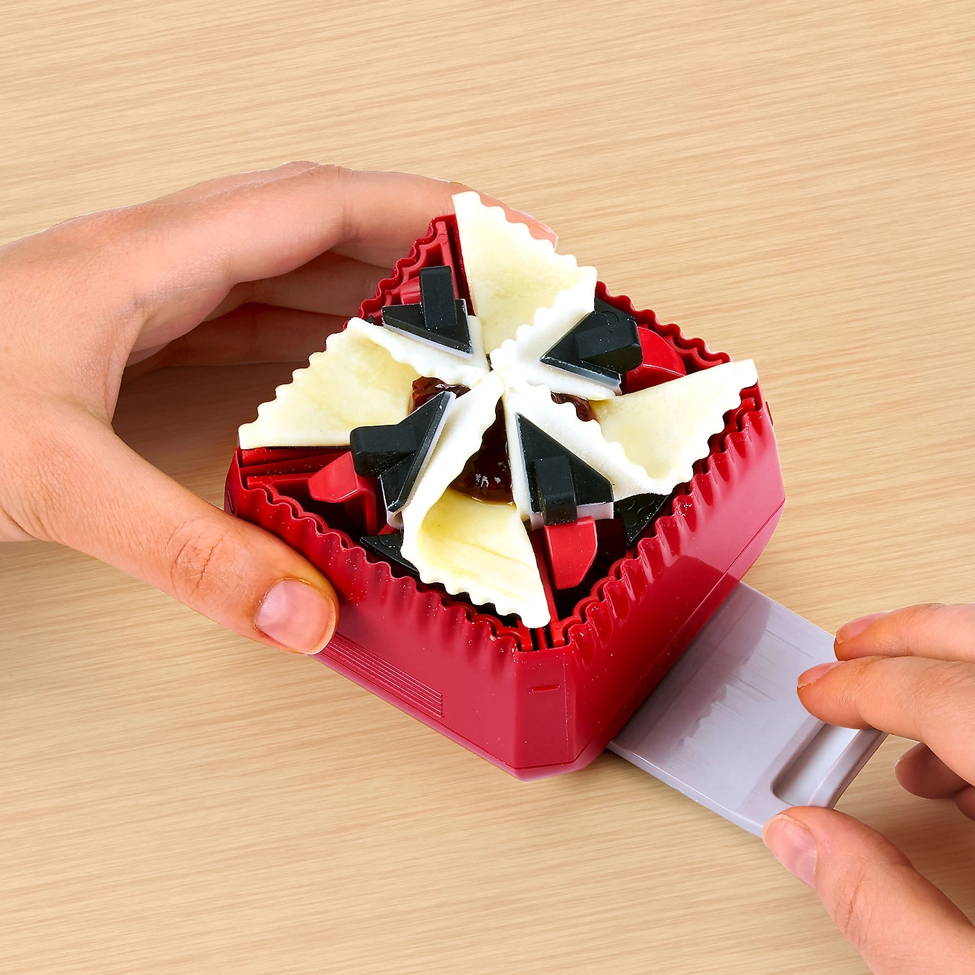 Hände halten rotes Werkzeug mit Kuchenstücken auf Holzoberfläche.