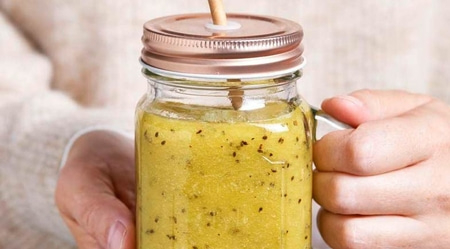 Un smoothie dans un bocal avec un couvercle et une paille, tenu par une personne.