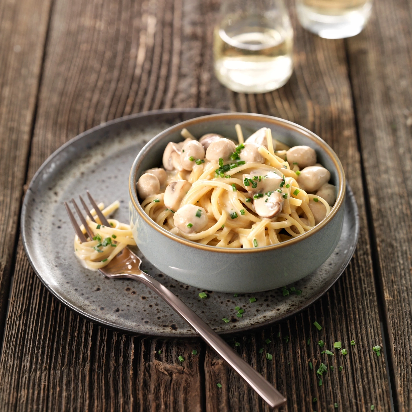 Pâtes aux champignons dans un bol sur une assiette avec une fourchette et du vin