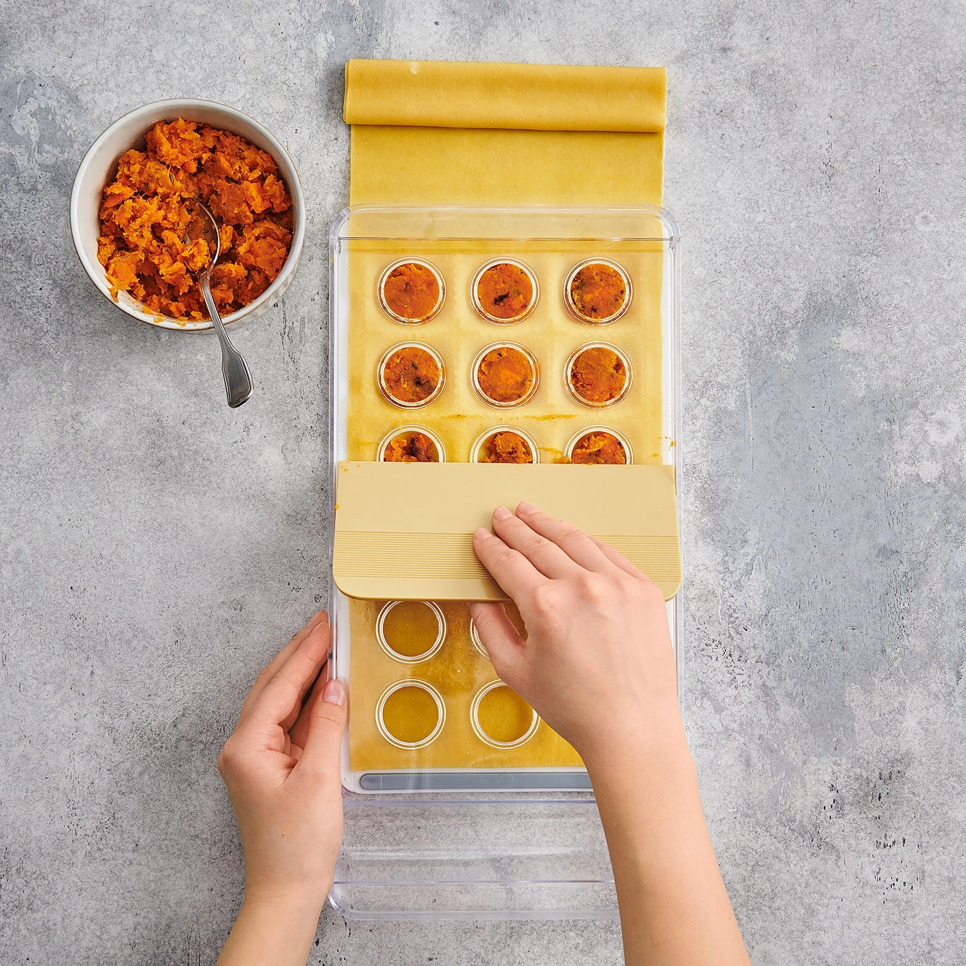 Personne faisant des raviolis avec garniture et outil sur fond gris.