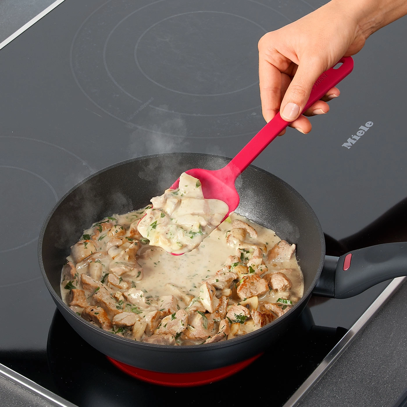 Person kocht in einer Pfanne. Fleisch und Soße werden mit einem Löffel verrührt.
