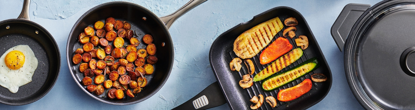 Pommes de terre sautées, légumes et œuf au plat dans des poêles sur fond bleu.