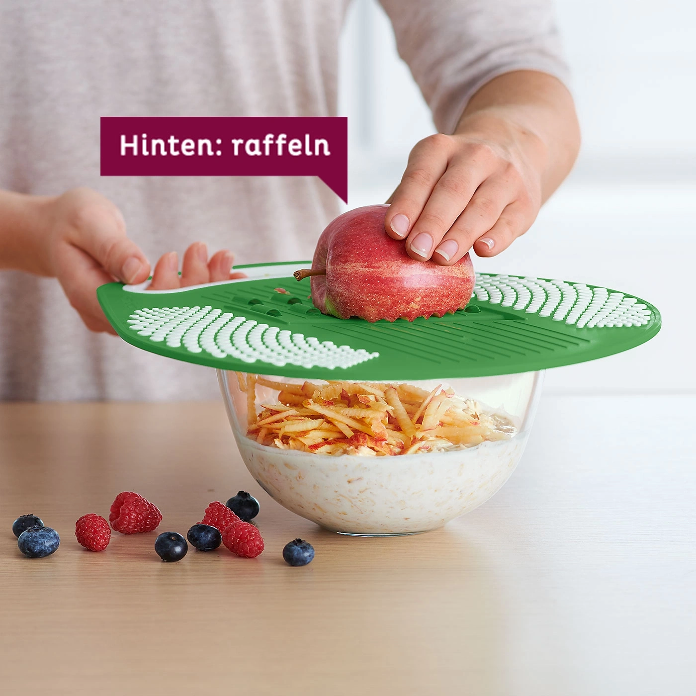 Apfel wird mit einer Reibe in eine Schüssel gerieben, mit Beeren garniert.