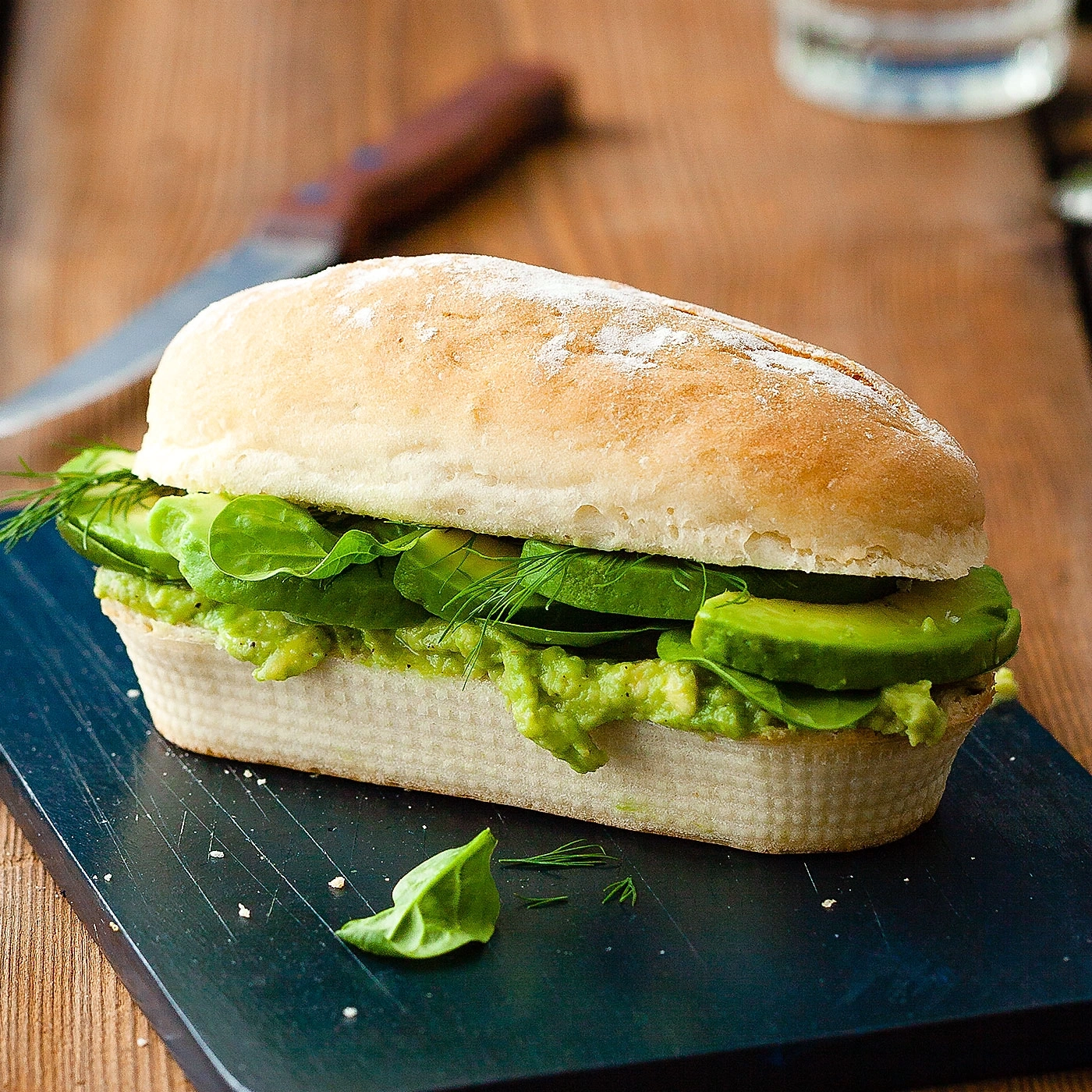 Avocado-Sandwich auf einem Holzbrett, mit Dill und Salat.