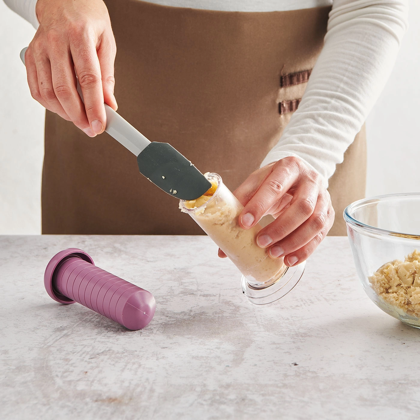 Une personne utilise une spatule pour mettre de la pâte dans un récipient, avec un autre récipient à côté.
