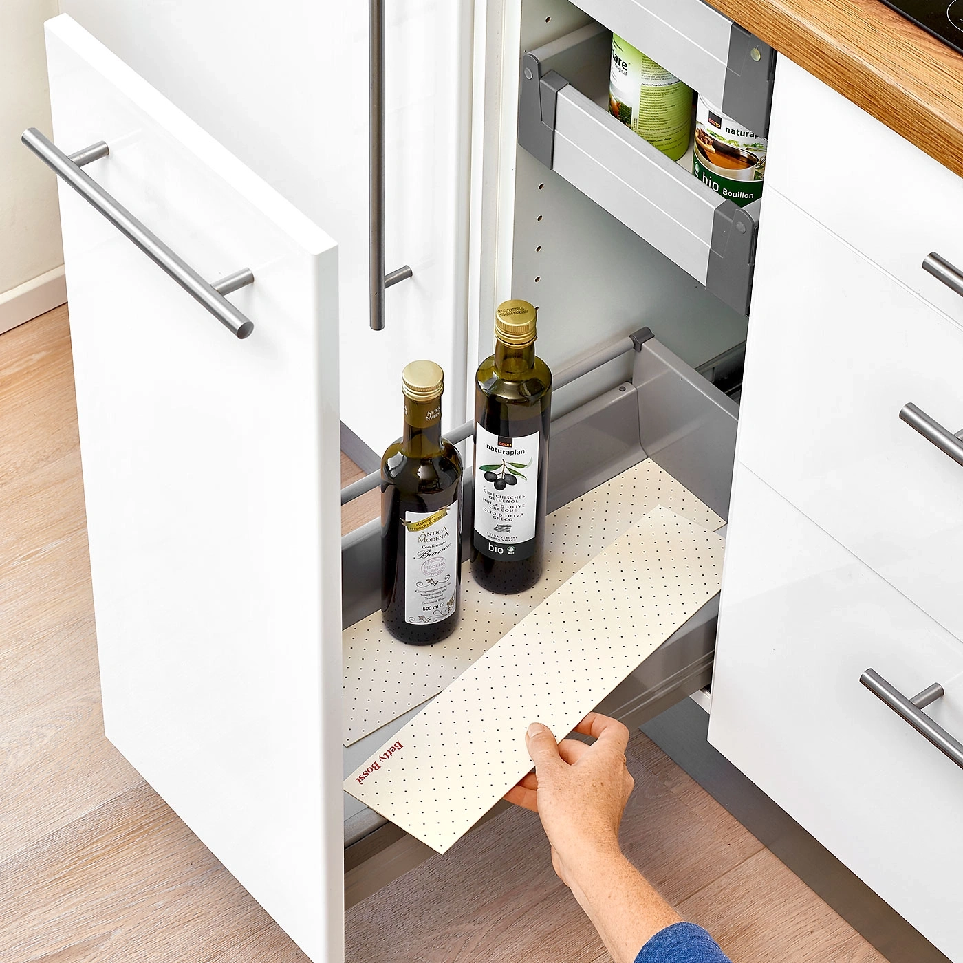 Armoire de cuisine avec bouteilles d'huile et tiroirs ouverts. Une main tient un tapis.