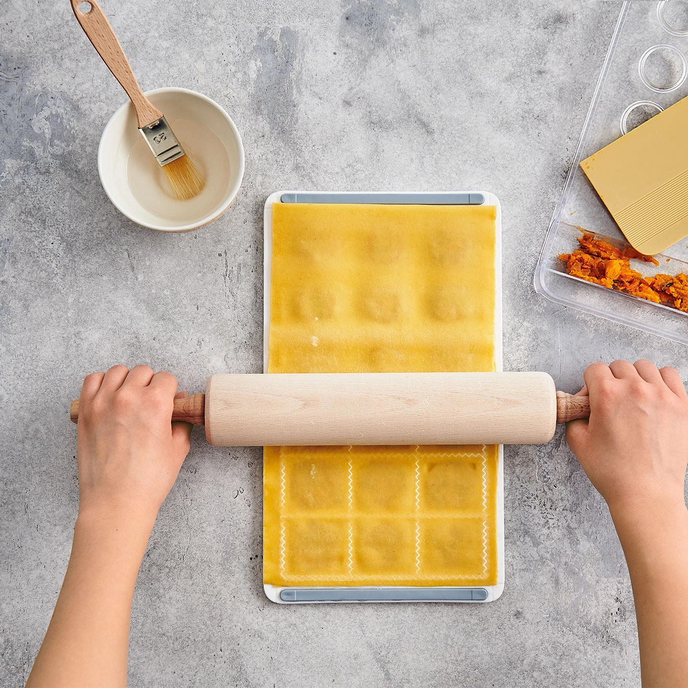 Mains roulant la pâte à pâtes avec un rouleau à pâtisserie sur une surface de travail avec des ingrédients.