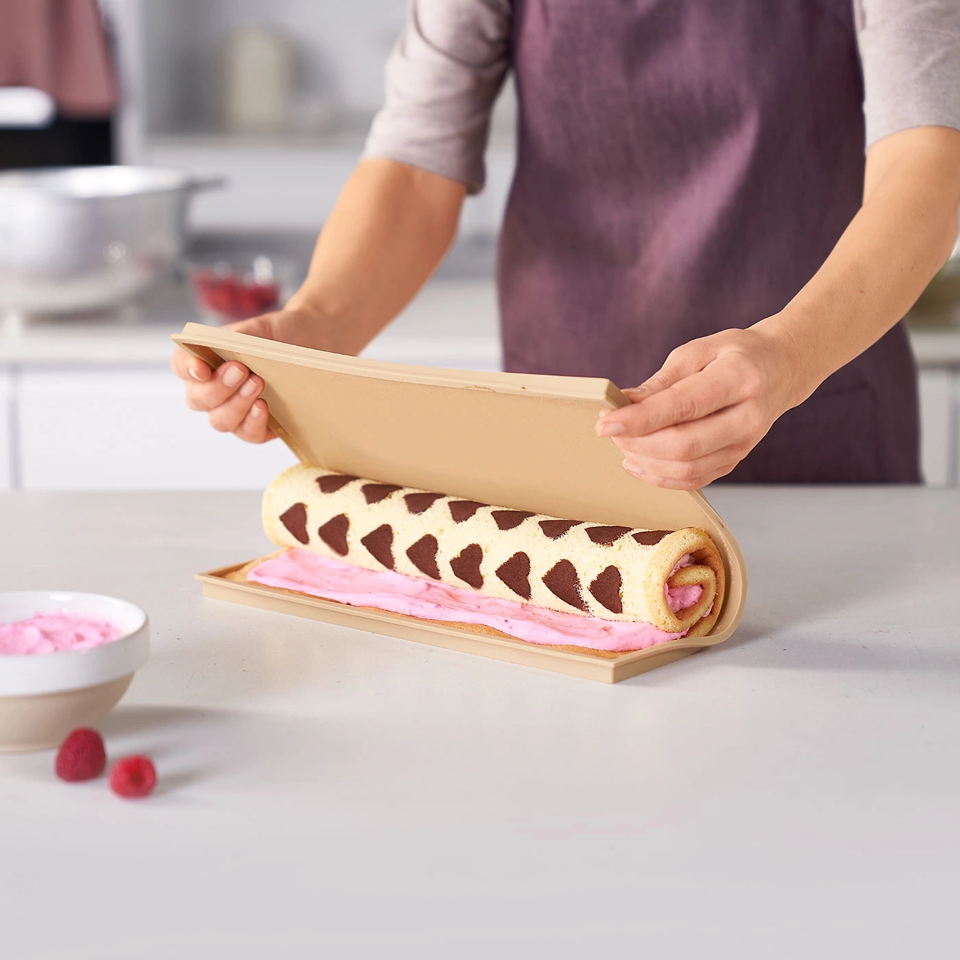 Personne tenant une roulade dans un moule, avec des framboises et de la crème.