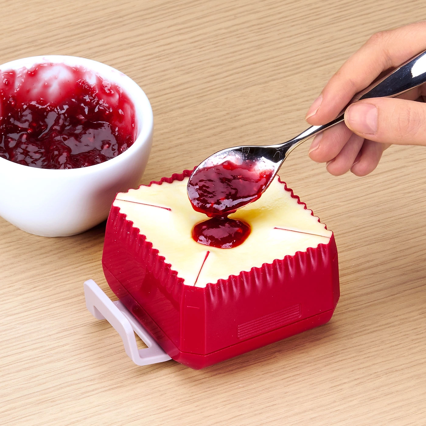 Jemand gibt Marmelade auf ein Käse-ähnliches Objekt mit einem Löffel.