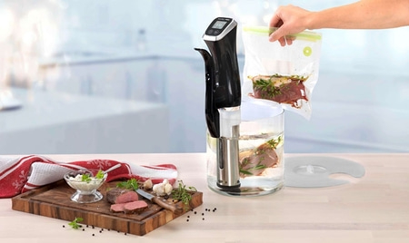 Sous-Vide-Gerät mit Fleisch und Zutaten, die in einem Wasserbad zubereitet werden.