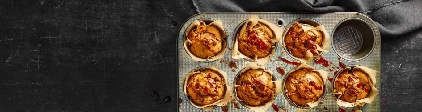 Muffins in einer Backform, auf einem dunklen Hintergrund, mit Sirup beträufelt.