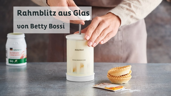 Personne tenant un fouet à crème en verre de Betty Bossi, avec pâtisseries et ingrédients.