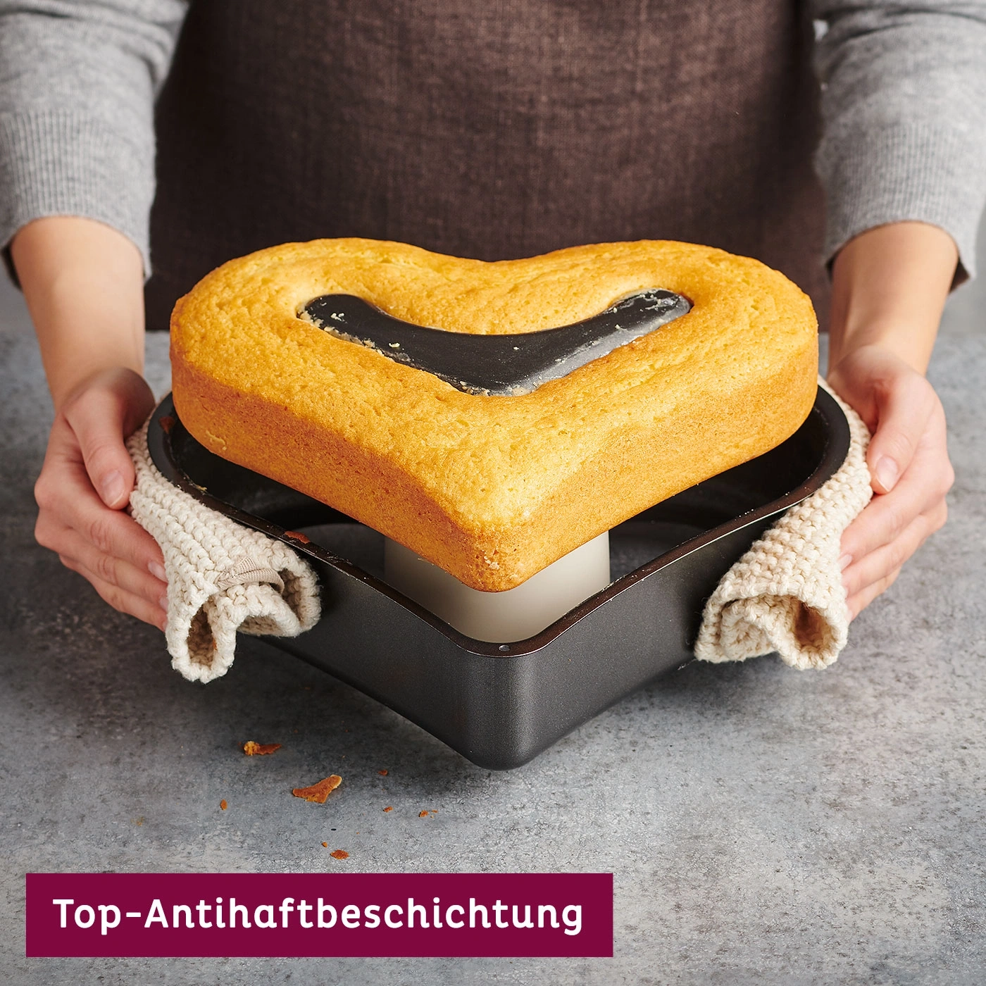 Herzförmiger Kuchen in Backform, gehalten von Händen, mit Text 'Top-Antihaftbeschichtung'