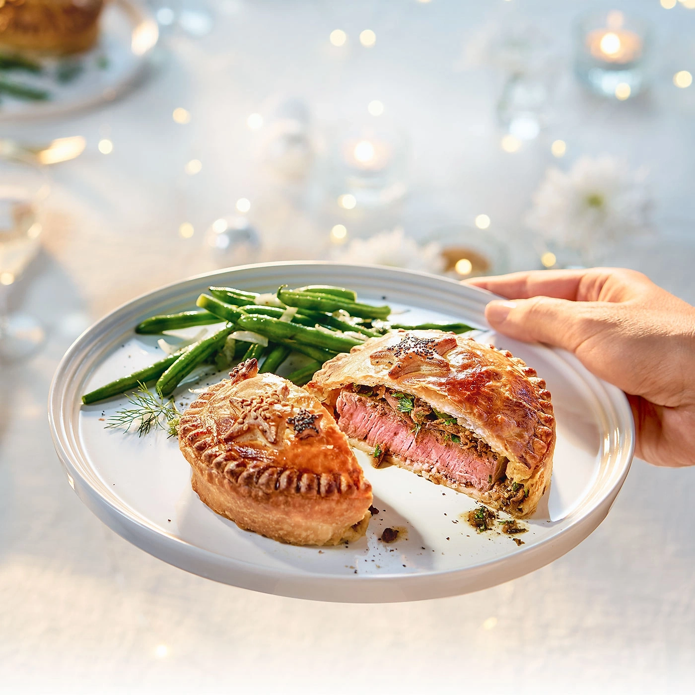 Plat de viande et haricots verts, tenu par une main, sur une table