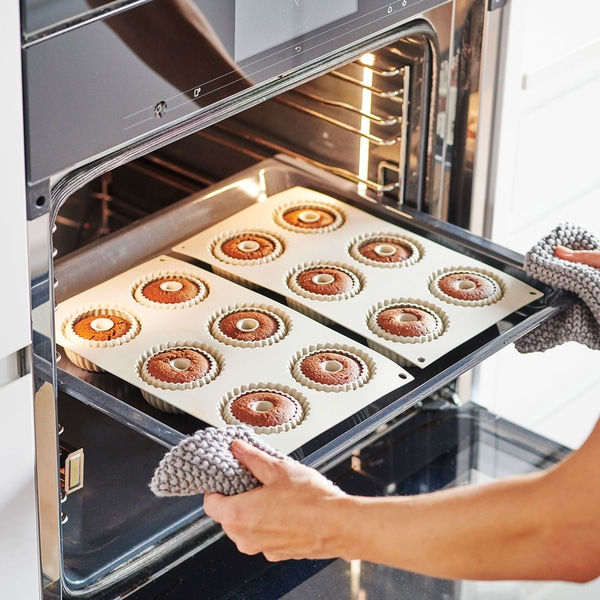 Backofen mit Kuchenformen. Person nimmt Kuchen aus dem Ofen.