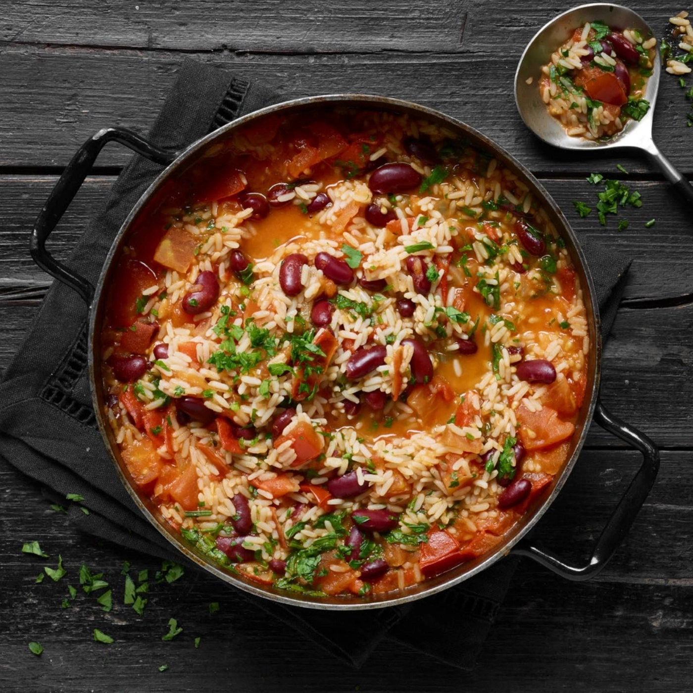 Plat de riz aux haricots rouges, tomates et herbes dans une poêle sur bois