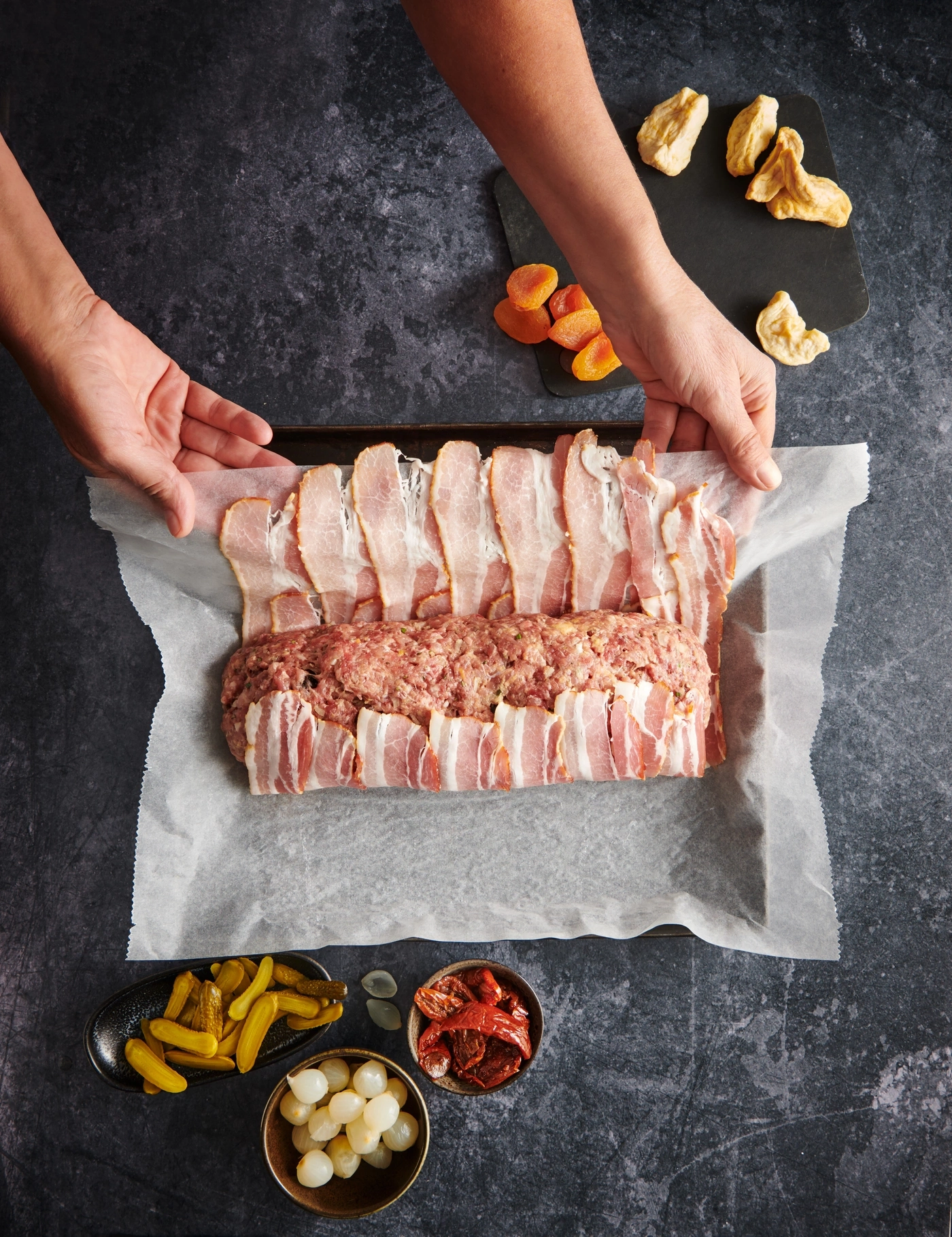 Fleischlaib mit Speck umwickelt, Zutaten, Hände, dunkler Hintergrund, Essen, Kochen