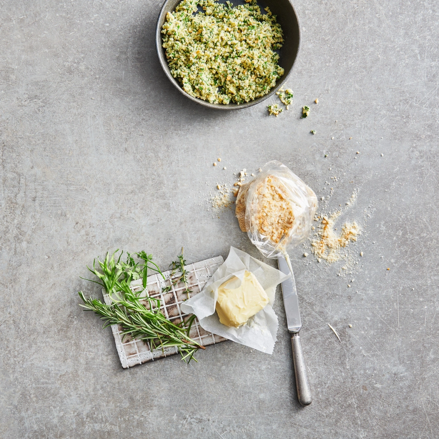 Schüssel mit Essen, Kräuter, Butter, Messer, Brot, auf grauem Hintergrund.
