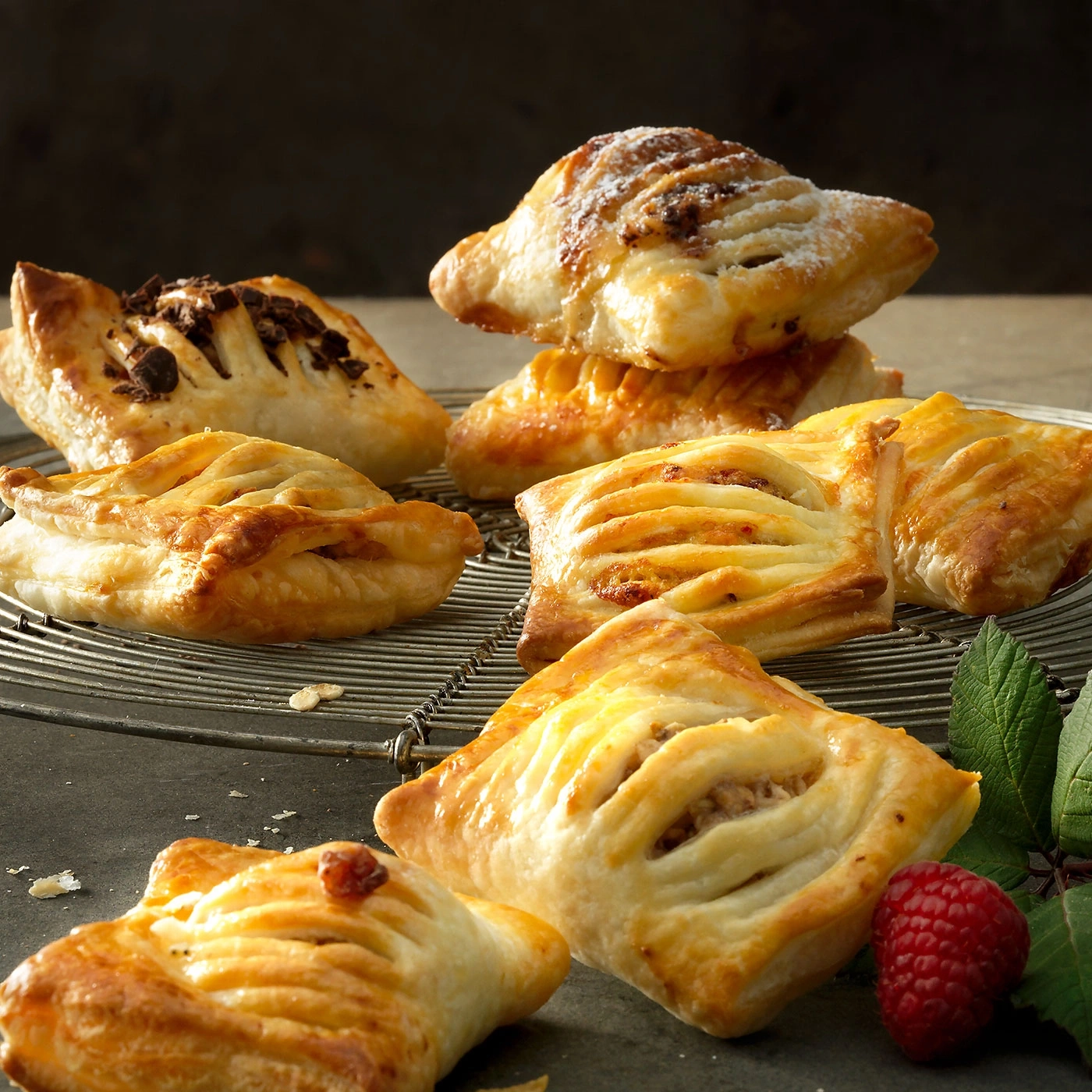 Assortiment de pâtisseries sur une grille métallique avec framboise et feuilles, gros plan