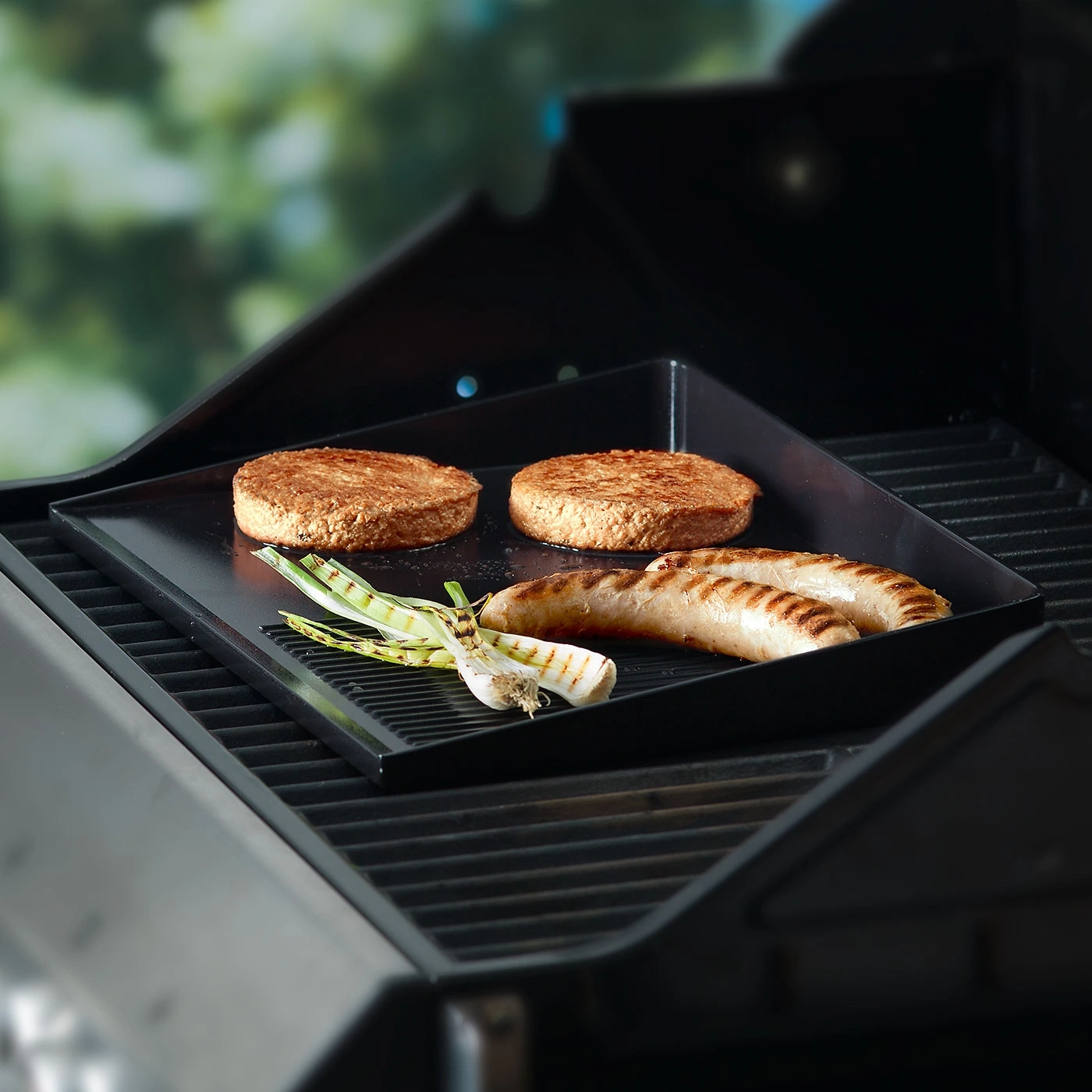 Gril avec saucisses, burgers et oignons sur une plaque noire.