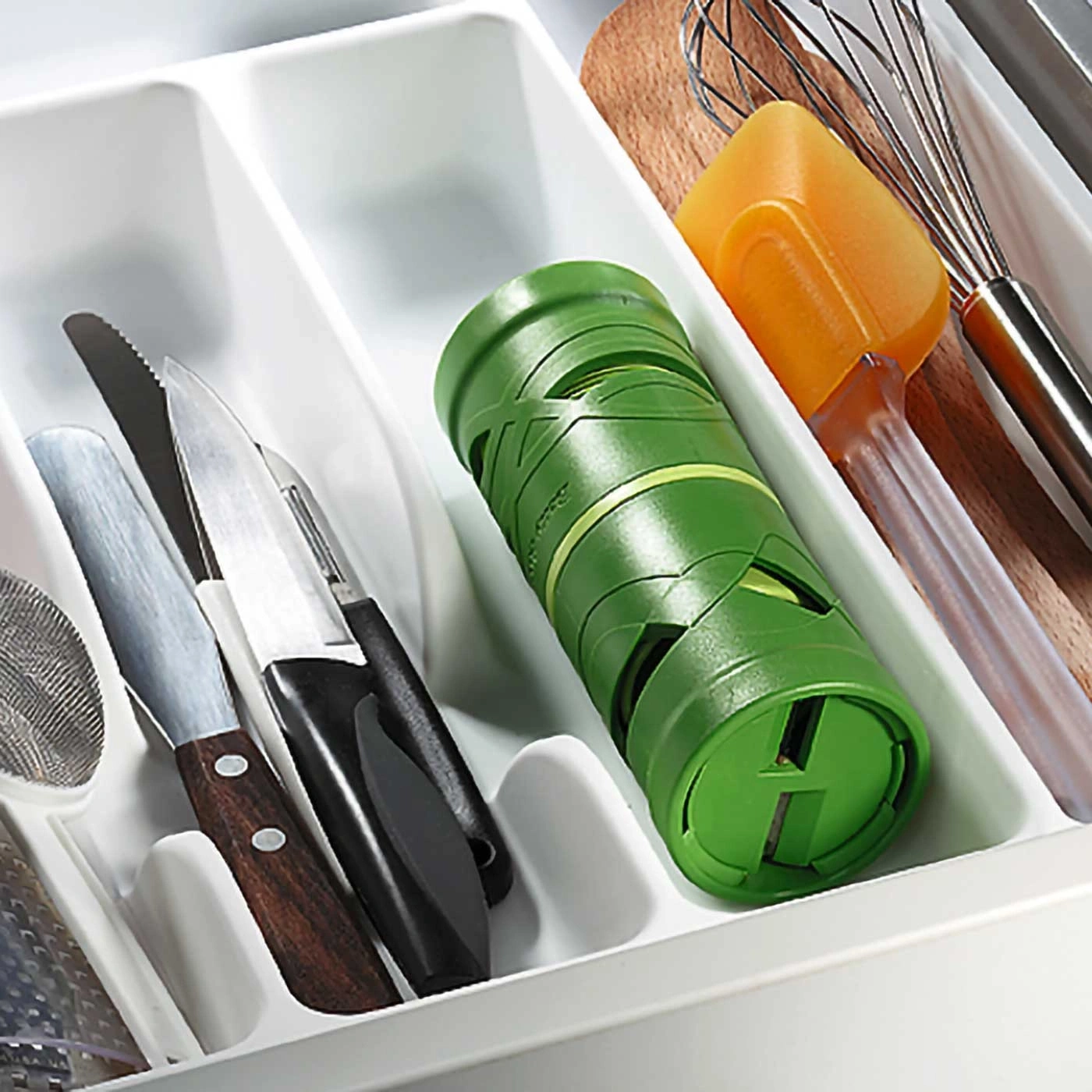 Küchenutensilien in einer Schublade: Messer, Spatel, Schneebesen, grüner Behälter.