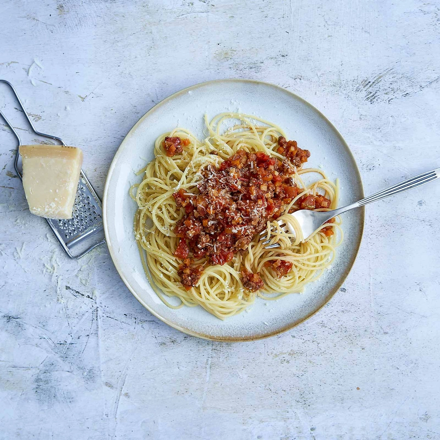 Spaghetti Bolognese mit Käse auf einem Teller mit Gabel und Käse.